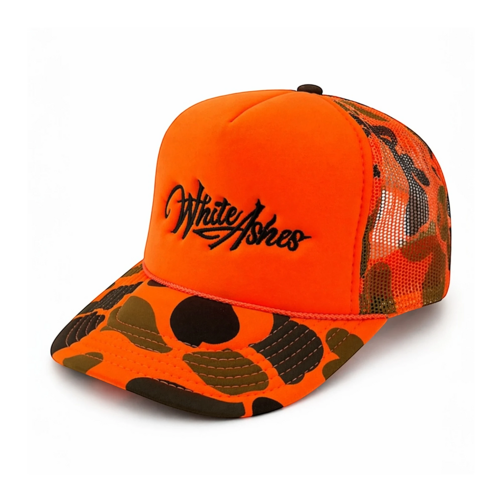 White Ashes Smoke Shop fire orange trucker hat with camo brim, mesh back, and espresso brown embroidered logo.