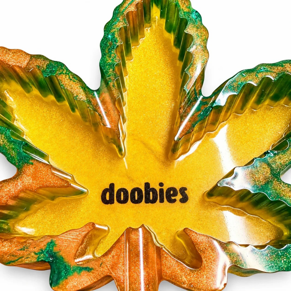 White Ashes Smoke Shop leaf-shaped resin ashtray in green, orange, and gold with the word doobies in the center.